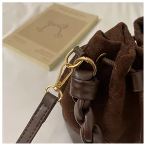 Close-up of gold-tone clasps, suede drawstring and braided leather handle on a brown bag