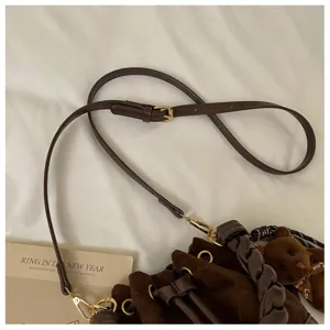 Close-up of the brown adjustable strap, gold-tone buckle and braided handle on the suede bag