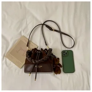 Flat lay of a brown patchwork bucket bag with braided handle, adjustable strap and teddy charm