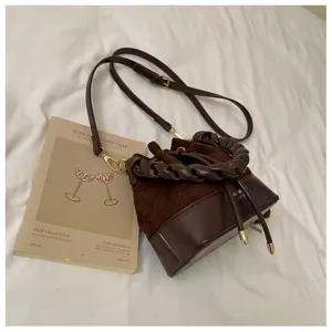 Overhead view of a brown bucket bag with braided handle and adjustable strap on white bedding