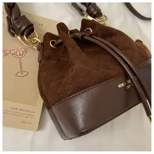 Close-up of brown suede texture, diamond stitching, drawstring, and gold-tone hardware on the bag