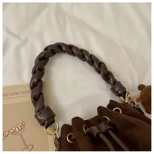 Brown suede-textured bag detail with diamond quilting, braided handle, gold hardware and bear charm