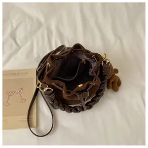 Top-down view of an open brown suede bucket bag with braided trim, drawstring and bear charm