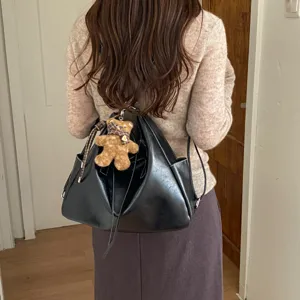 Rear view of a model carrying a glossy black drawstring bag with a plush bear charm