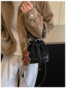 Detail of a black suede bucket bag worn crossbody, with a leather base, drawstring and teddy charm
