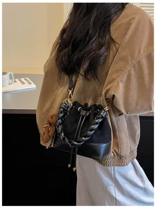 Back view showing a black quilted bag with braided handle, drawstring top and teddy bear charm