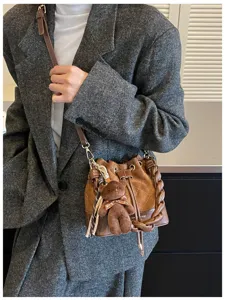 Close-up of a brown quilted bucket bag with braided handle, shoulder strap and teddy bear charm