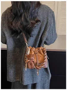 Back view of a brown suede bucket bag with braided handle and teddy charm worn over a coat