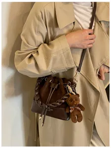 Brown quilted bucket bag with chain handle and teddy charm styled over a beige trench coat