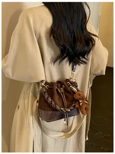 Brown quilted bucket bag worn over the shoulder, with a braided handle and teddy bear charm