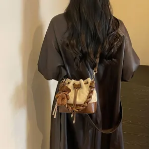 Beige and brown quilted bucket bag with braided handle and bear charm, worn crossbody from the back