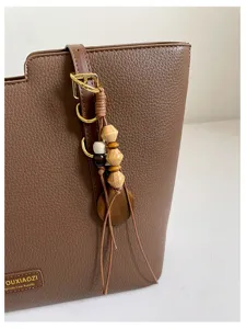 Gros plan sur un sac marron grainé, avec des ferrures dorées et un pompon de perles en bois