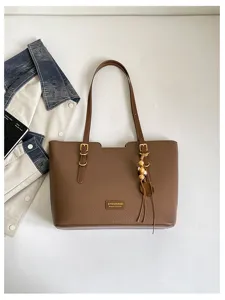 Détail d’un sac marron à texture grainée, avec boucles dorées et pendentif orné de perles de bambou