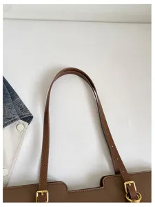 Gros plan sur les anses brunes du sac, les boucles dorées et la texture du similicuir grainé