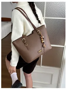 Sac brun à texture grainée, avec boucles dorées et breloque en perles de bois, porté à l’épaule