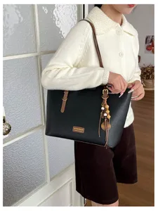 Porté par un modèle, sac noir à anses en cuir brun, boucles métalliques et breloque en bois
