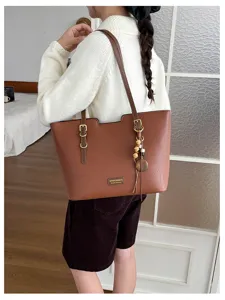 Vue portée d’un cabas marron texturé sur l’épaule, avec boucles dorées et pendentif à perles