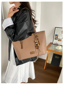 Sac marron porté à l’épaule, avec texture grainée, fermoir métallique et breloque en perles