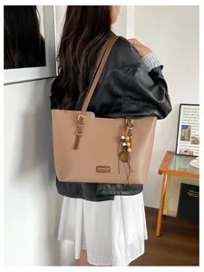 Femme portant un cabas beige texturé, avec attaches métalliques sur les anses et breloque en bois