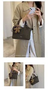 Model carrying a brown suede tote with leather handles, a metal accent and a plush bear charm