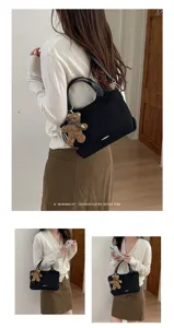 Model wearing a black suede-look handbag with a teddy bear charm, shown over the shoulder