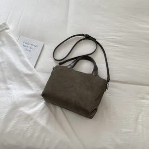 Olijfbruine suèdelook tas met donkere handvatten en riem, plat gefotografeerd op witte stof