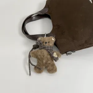 Bruine pluchen berenhanger met geruite strik en hartlabel naast een tas in suèdelook