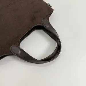 Detail van een donkerbruine suède-look tas, met gebogen imitatieleren handvat en nette stiksels