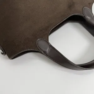 Close-up van de donkerbruine suède tastextuur, leren hengselrand en nette, gelijkmatige stiksels