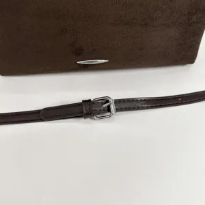 Close-up van de donkerbruine suède-look tasrand en smalle riem met zilverkleurige gesp