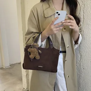 Een model draagt een bruine suède-look shopper met donkere handvatten en een hangende berenhanger