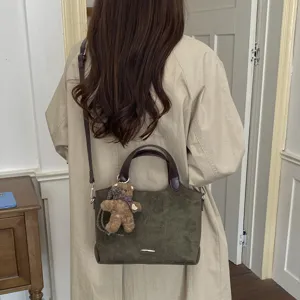 Olijfgroene suèdetas crossbody gedragen, met donkere handvatten en bruine teddybeerhanger
