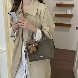 Olijfbruine tas met suède-look, donkere handvatten en teddybeerhanger, gedragen door een model