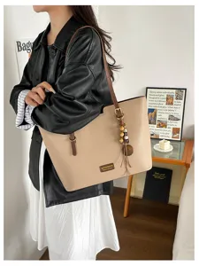 Vue portée d’un cabas beige texturé, avec bandoulière marron et breloque en perles de bois