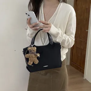 Zwarte tas met suède-look, leren handvatten, zilveren sierstrip en bruine berenhanger.