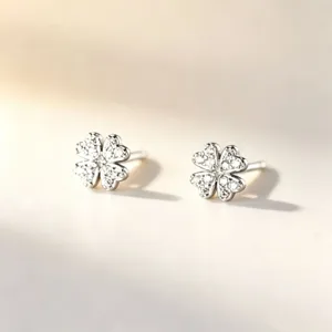 Paire de puces en forme de trèfle, ornées de pierres claires scintillantes sur un fond ivoire doux