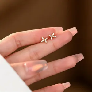 Puces d’oreilles dorées en fleur à quatre pétales, ornées de petites pierres blanches, sur les doigts