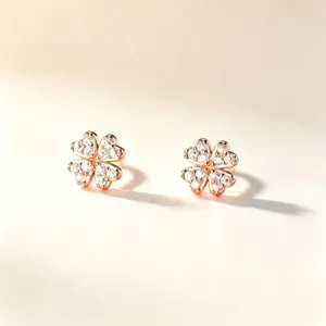Paire de clous en forme de trèfle, dorés rose et ornés de pierres claires, sur fond ivoire doux