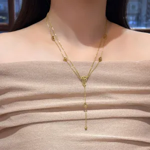 Close-up of layered gold Y necklace with oval links and a bead drop, worn over a beige top