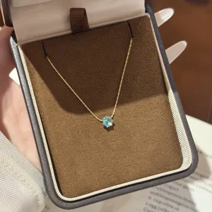 Gold chain with a round blue gemstone pendant displayed in a dark brown velvet jewelry box