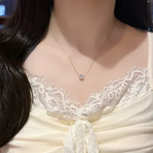 Close-up of a delicate gold-tone necklace with a square clear pendant worn against a lace top