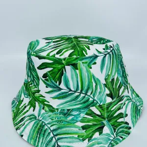 White bucket hat with layered tropical green leaf print and stitched brim, displayed on gray