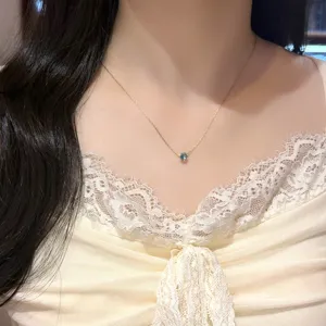 Fine gold-tone necklace worn at the neck, with a small blue faceted pendant over a lace top