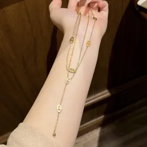 Close-up of a gold-tone layered chain with open oval charms and a small ball pendant, displayed on a hand