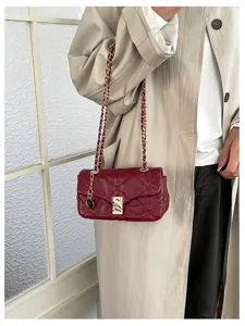 Borsa bordeaux trapuntata con patta, catena e chiusura dorate, indossata su un trench beige