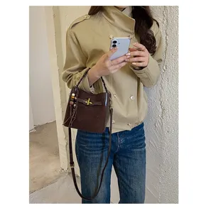 Brown bucket bag worn crossbody, featuring a woven handle, wooden bead charm and long strap
