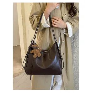 A dark brown bag hangs from a beige coat, with a long shoulder strap and teddy bear charm