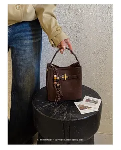 Model holding a dark brown bag by its braided handle, with gold clasp and wooden bead tassel