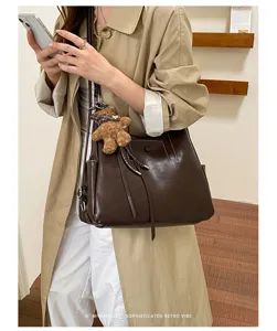 Lifestyle view of a dark brown faux-leather shoulder bag with teddy charm, worn with a beige coat
