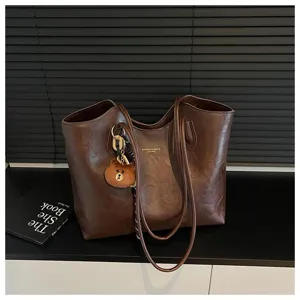 Braune Kunstledertasche mit Doppelgriffen und kleinem Bärenanhänger auf schwarzer Tischfläche